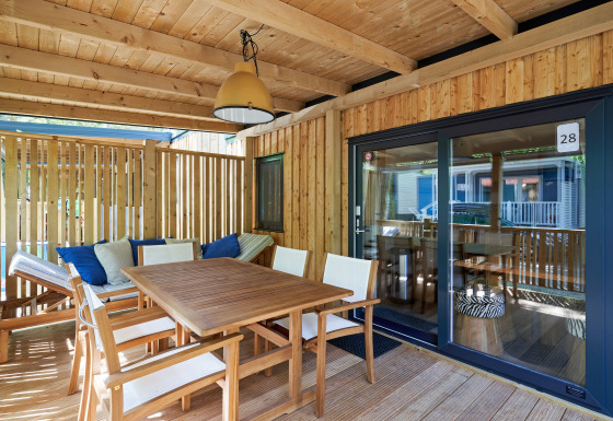 Solrig træterrasse på SunLodge Katsura med spisebord, stole og bænk med puder under overdækning.