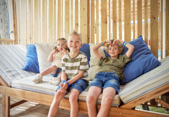 Tre bambini rilassati su una panca nella SunLodge Katsura presso hu Park Albatros Village in Italia.