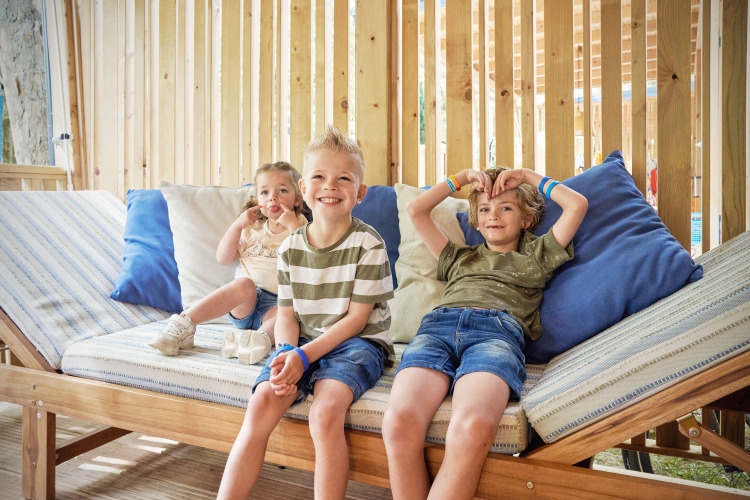 Tres niños relajados en un banco dentro de SunLodge Katsura en hu Park Albatros Village, Italia.