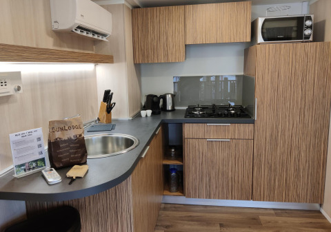 Angolo cottura moderno alla SunLodge Katsura con mobili in legno, fornello a gas, microonde e utensili.