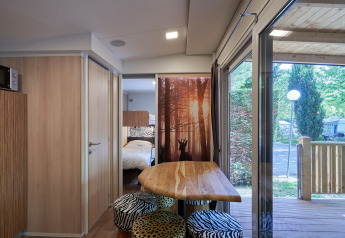 Binnenaanzicht van SunLodge Katsura met houten tafel, dierenprint krukken en toegang tot het terras.