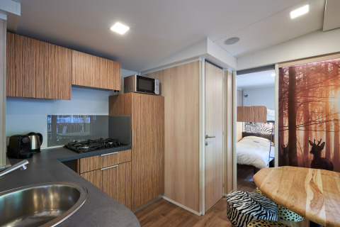 Moderne keuken in SunLodge Katsura met houten kasten, eettafel en zicht op slaapkamer en bosafbeelding.