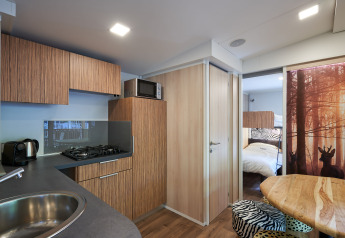 Moderne keuken in SunLodge Katsura met houten kasten, eettafel en zicht op slaapkamer en bosafbeelding.