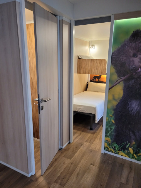 Kamer in SunLodge Katsura met houten vloer, open deur, bed en een muurdecoratie met een beer.