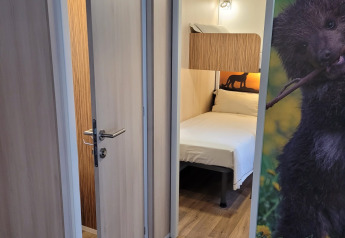 Chambre à SunLodge Katsura avec sol en bois, porte ouverte, lit et décoration murale d’ours.