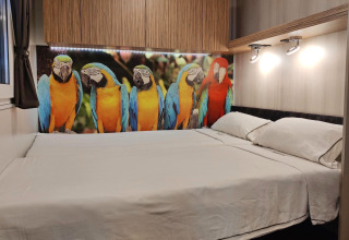 Dormitorio en SunLodge Katsura con cama doble, gabinetes de madera y mural de guacamayos coloridos en la cabecera.