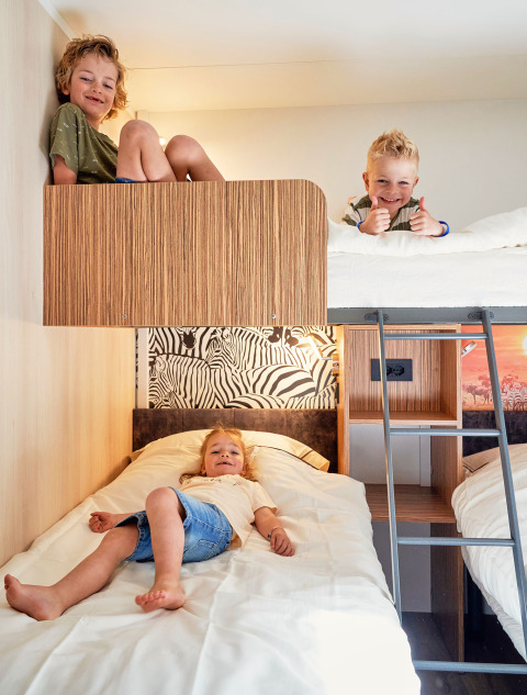 Drie kinderen spelen en rusten op stapelbedden in een gezellige lodge bij SunLodge Katsura, hu Park Albatros Village, Italië.