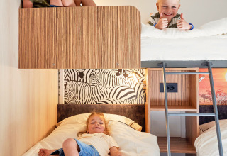 Tres niños juegan y descansan en literas dentro de una acogedora cabaña en SunLodge Katsura, hu Park Albatros Village, Italia.