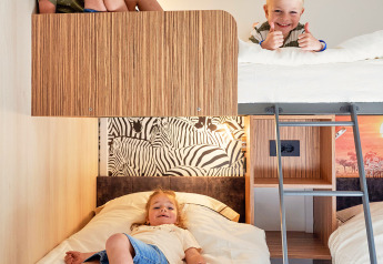 Drie kinderen spelen en rusten op stapelbedden in een gezellige lodge bij SunLodge Katsura, hu Park Albatros Village, Italië.