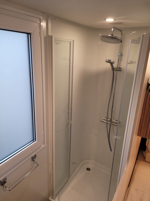 Cabina doccia moderna con soffione a pioggia vicino a finestra opaca al SunLodge Katsura, luminosa e pulita.