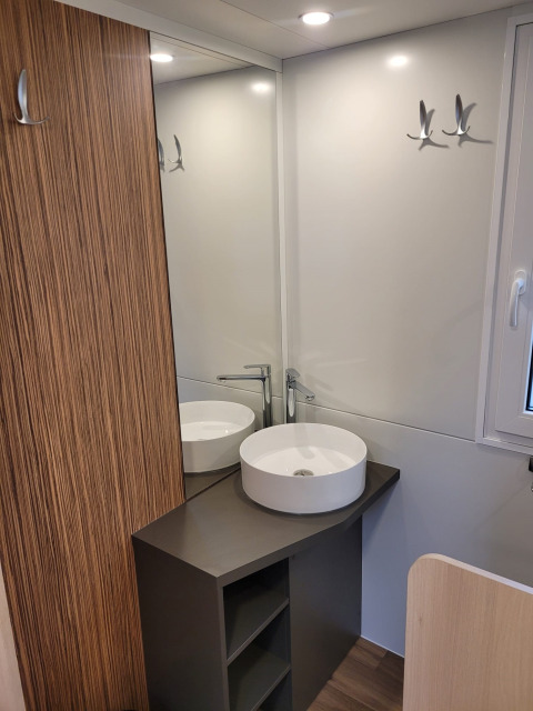 Moderne badkamer in SunLodge Katsura met ronde waskom, spiegel, houtpanelen en kapstokken.