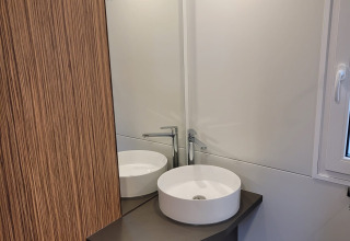 Baño moderno en SunLodge Katsura con lavabo redondo, espejo, panel de madera y percheros.