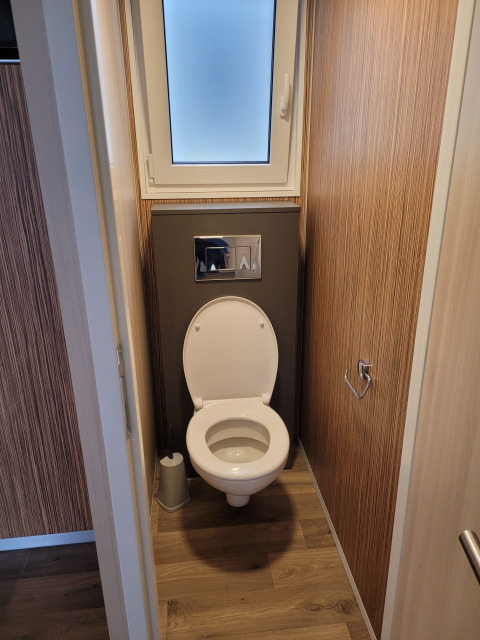 Moderne wc in een smalle houten badkamer bij SunLodge Katsura met matglasraam erboven.