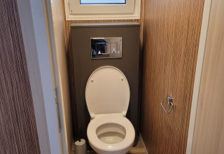 Inodoro moderno en un baño estrecho de madera en SunLodge Katsura con ventana esmerilada arriba.
