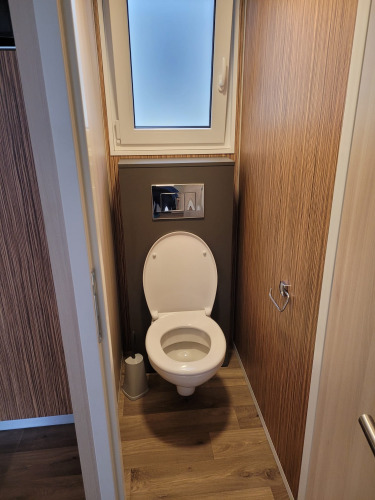 Inodoro moderno en un baño estrecho de madera en SunLodge Katsura con ventana esmerilada arriba.