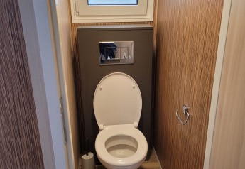 Inodoro moderno en un baño estrecho de madera en SunLodge Katsura con ventana esmerilada arriba.