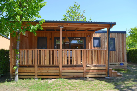 Vista esterna della SunLodge Sabai, una casetta di legno con veranda coperta immersa nel verde e negli alberi.