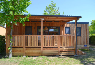 Vista esterna della SunLodge Sabai, una casetta di legno con veranda coperta immersa nel verde e negli alberi.
