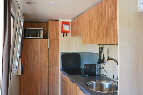 Compacte keukenhoek in SunLodge Sabai met spoelbak, microgolfoven, houten kasten en keukengerei.