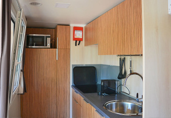 Compacte keukenruimte in SunLodge Sabai met gootsteen, magnetron, houten kasten en keukengerei.