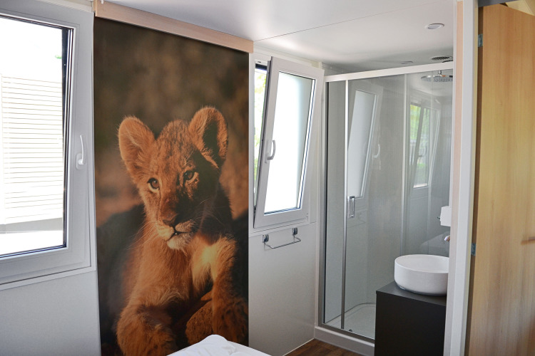 Baño moderno en SunLodge Sabai con ducha de vidrio y gran póster de un cachorro de león cerca de la cama.