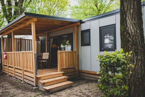 Ingresso alla SunLodge Sabai, con una cabina moderna, veranda in legno coperta, sedie e alberi intorno.