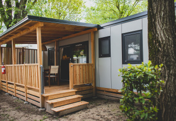 Entrance to SunLodge Sabai, featuring a modern cabin with a covered wooden porch, chairs, and trees around.
