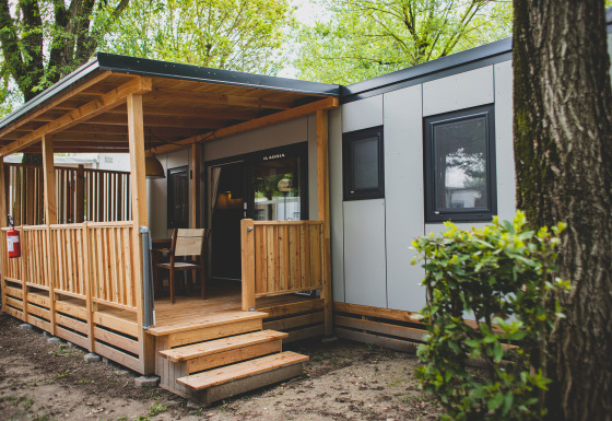 Ingang van SunLodge Sabai, moderne hut met overdekt houten terras, stoelen en bomen eromheen.