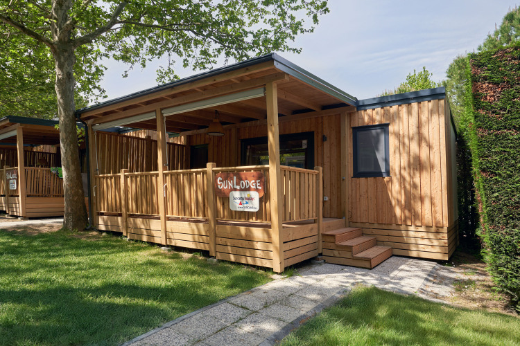 SunLodge Katsura wooden cabin with porch, surrounded by trees and green grass in a peaceful setting.