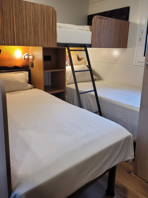Camera al SunLodge Katsura con letto a castello e due singoli, arredamento moderno in legno e lenzuola bianche.