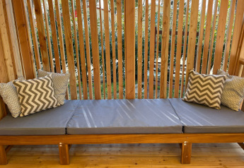 Banc en bois extérieur avec coussins gris et oreillers à motifs à SunLodge Babul, entouré de lattes.