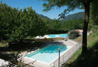 Due piscine circondate da alberi e montagne al Camping Il Collaccio, parco vacanze in Umbria, Italia.