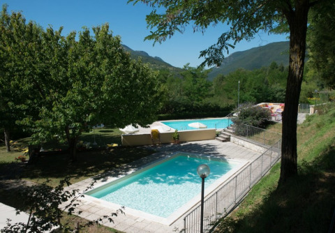 Due piscine circondate da alberi e montagne al Camping Il Collaccio, parco vacanze in Umbria, Italia.