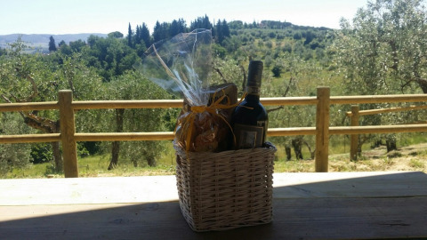 Cesto regalo con vino e snack su un tavolo di legno con vista colline toscane ad Agricamping Romita, Italia.