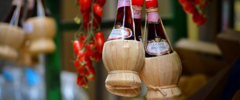 Bottiglie di vino Chianti in fiaschi di paglia appese con pomodori in un mercato tipico toscano in Italia.
