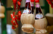 Bottiglie di vino Chianti in fiaschi di paglia appese con pomodori in un mercato tipico toscano in Italia.