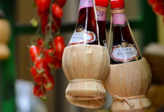 Bottiglie di vino Chianti in fiaschi di paglia appese con pomodori in un mercato tipico toscano in Italia.
