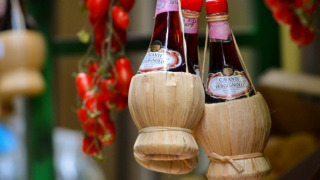 Bottiglie di vino Chianti in fiaschi di paglia appese con pomodori in un mercato tipico toscano in Italia.