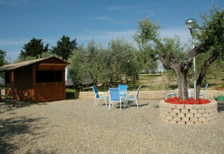Vista di Agricamping Romita in Toscana, Italia, con tavolo, sedie da esterno, piante e casetta di legno.