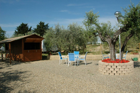 View of Agricamping Romita holiday park in Tuscany, Italy with outdoor seating, trees, and a wooden cabin.