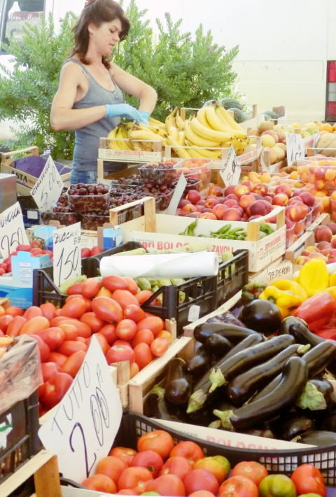 Mujer vendiendo frutas y verduras frescas en un mercado local en Agricamping Romita, Toscana, Italia.