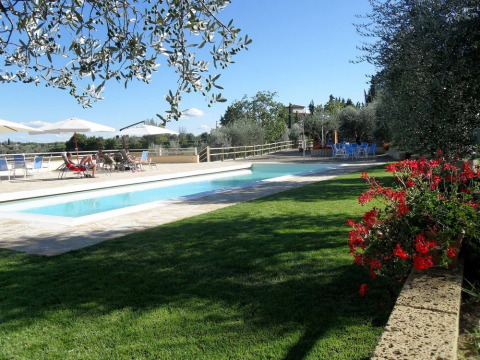 Piscina al aire libre con tumbonas, sombrillas y flores en Agricamping Romita en la Toscana, Italia.