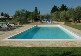Piscina con lettini e tavolini immersa nel verde presso Agricamping Romita nelle campagne toscane, Italia.