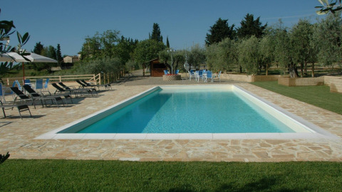 Piscina con lettini e tavolini immersa nel verde presso Agricamping Romita nelle campagne toscane, Italia.