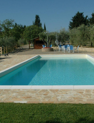 Piscina con lettini e tavolini immersa nel verde presso Agricamping Romita nelle campagne toscane, Italia.