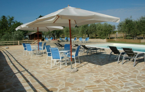 Area piscina con ombrelloni e sedie blu presso Agricamping Romita, parco vacanze in Toscana, Italia.