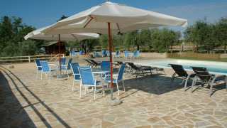 Area piscina con ombrelloni e sedie blu presso Agricamping Romita, parco vacanze in Toscana, Italia.