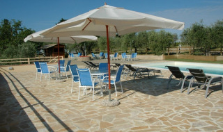 Area piscina con ombrelloni e sedie blu presso Agricamping Romita, parco vacanze in Toscana, Italia.