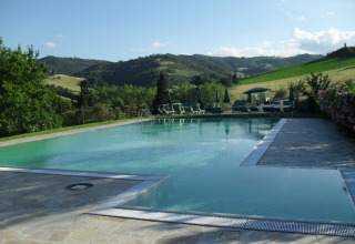 Svømmebassin ved Camping Podere sei Poorte, omgivet af liggestole og bakker i Marche, Italien.