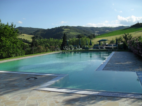 Piscina en Camping Podere sei Poorte, rodeada de tumbonas y colinas en Marche, Italia.